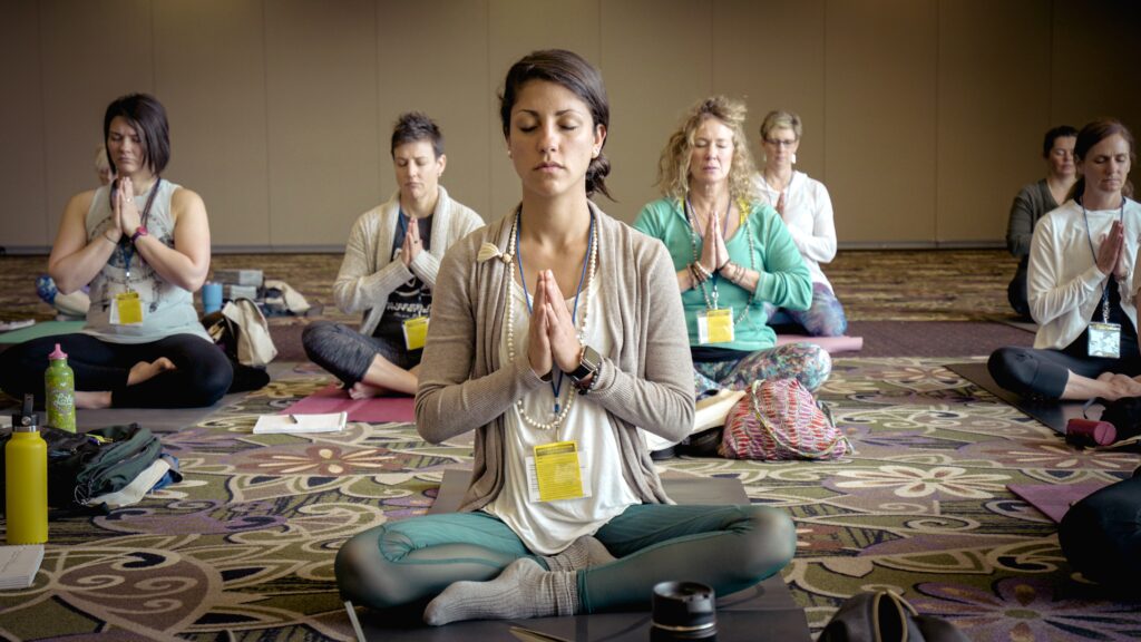 Un groupe de femme  pratique le yoga dans une salle de yoga dirigé par une proffesseur de yoga. 